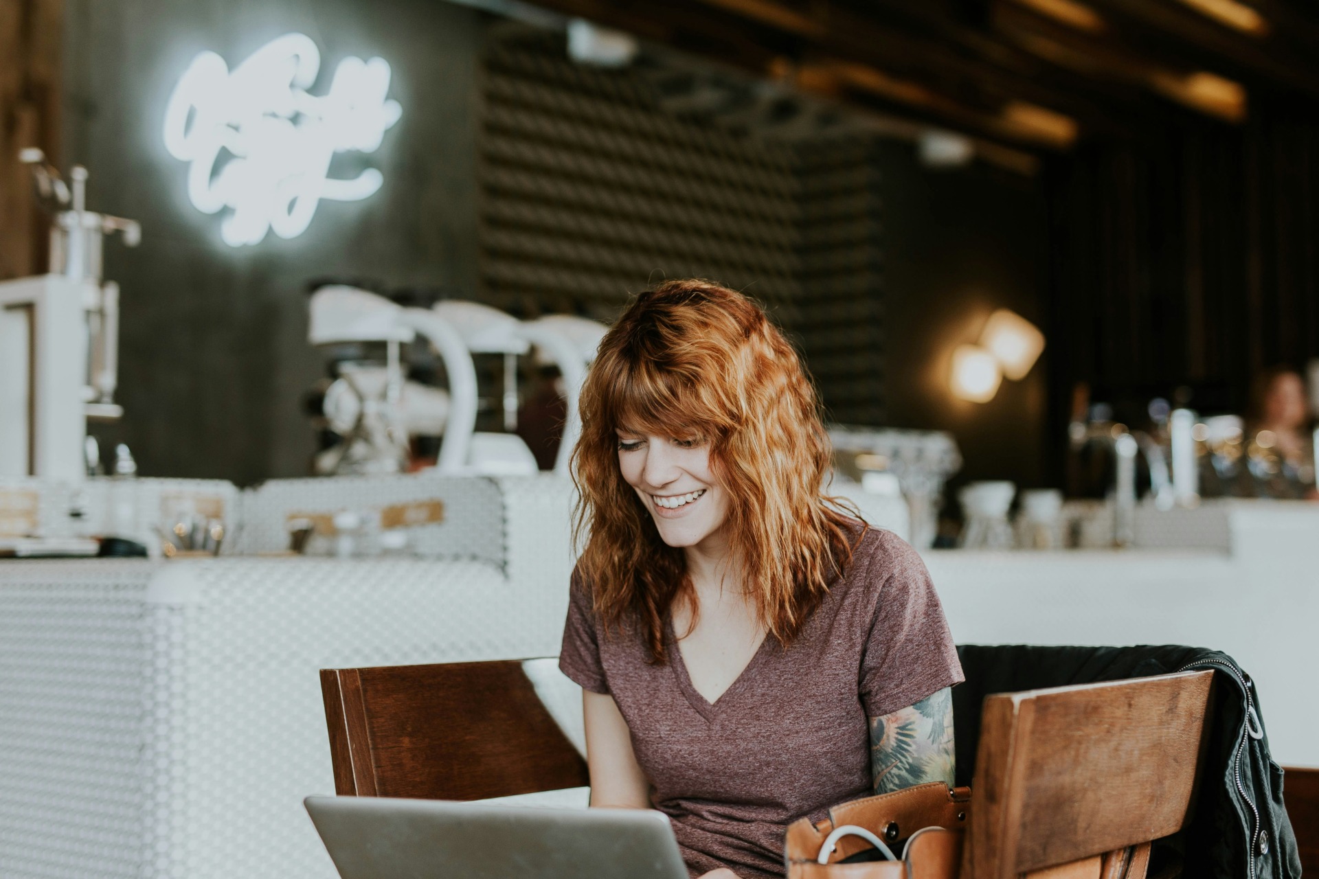 Lächelnde Frau mit roten Haaren arbeitet entspannt am Laptop in einem Café – sie fühlt sich mit ihrer Website wieder stimmig