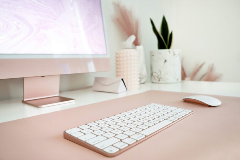 Aufgeräumter rosafarbener Schreibtisch mit Monitor und Tastatur