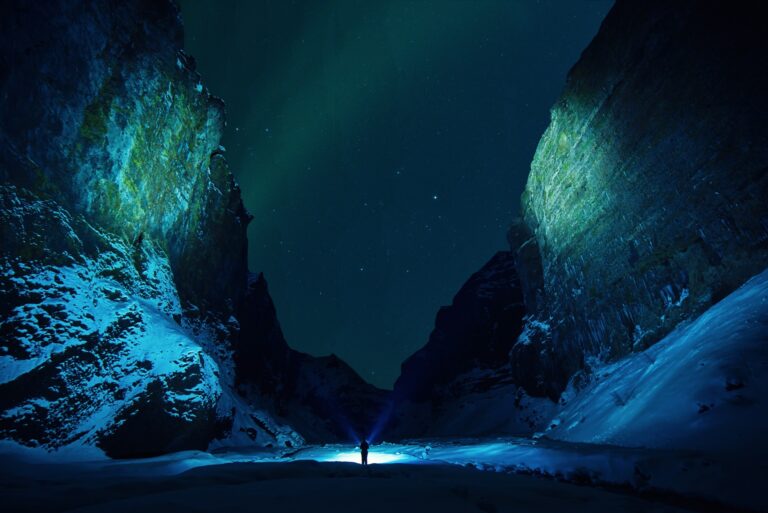 Person mit Lampe zwischen dunklen Felsen unter grünem Polarlicht
