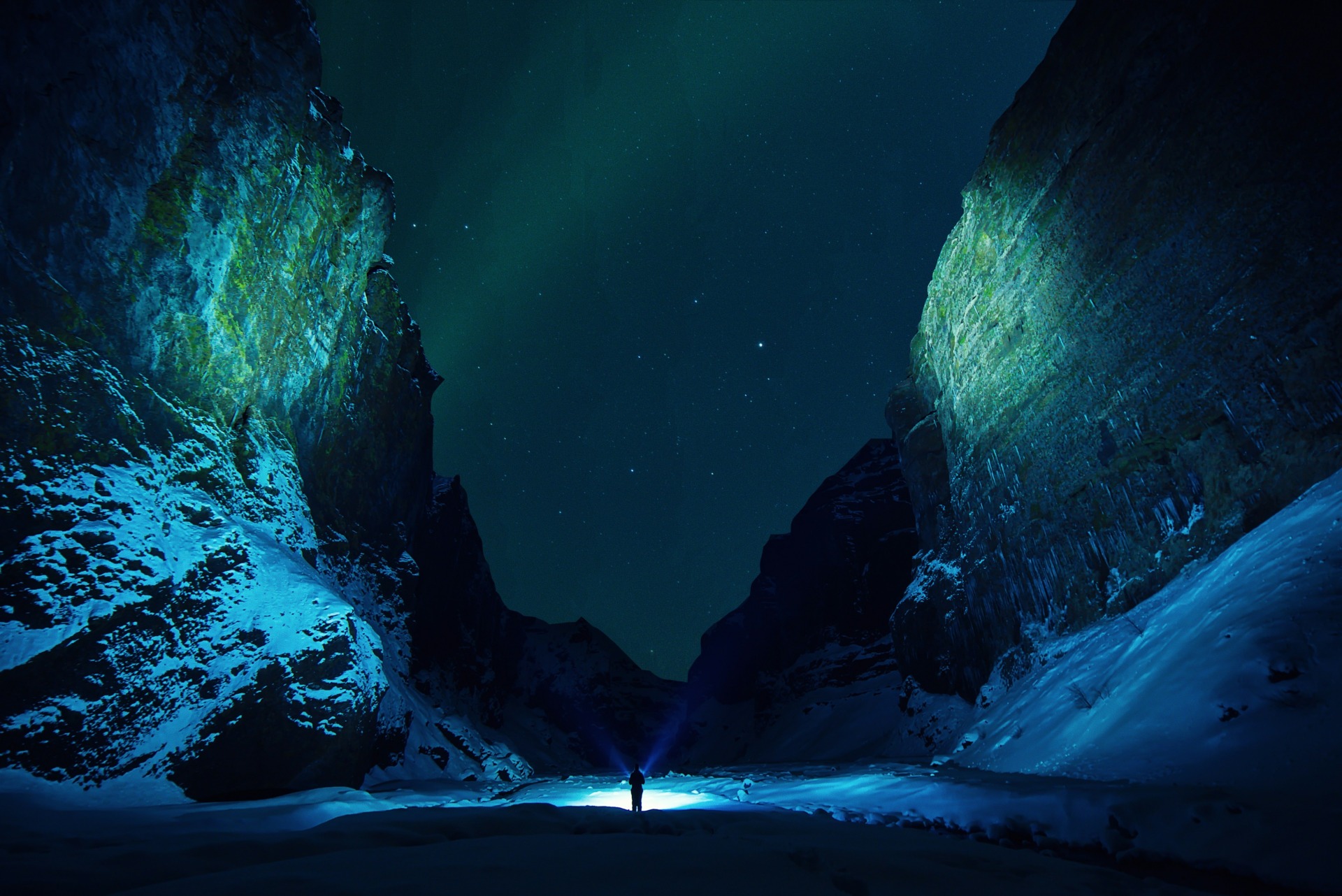 Person mit Lampe zwischen dunklen Felsen unter grünem Polarlicht