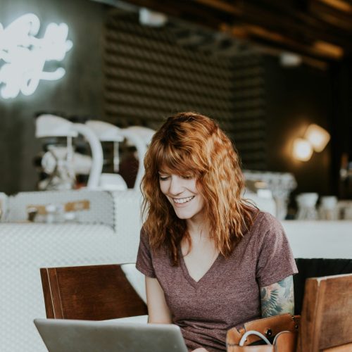 Lächelnde Frau mit roten Haaren arbeitet entspannt am Laptop in einem Café – sie fühlt sich mit ihrer Website wieder stimmig