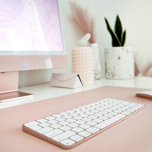 Aufgeräumter rosafarbener Schreibtisch mit Monitor und Tastatur